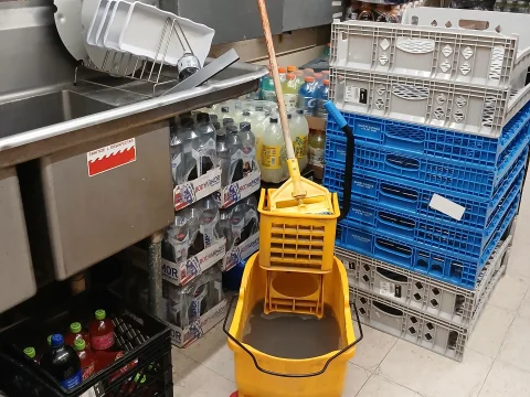 Yellow mop bucket and cleaning supplies in a storage room